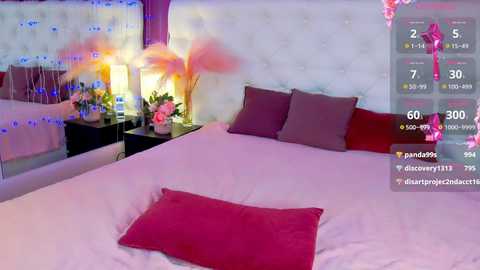 Media: Video of a modern, pink-themed bedroom with a white tufted headboard, two pillows, a red throw pillow, and a pink vase with flowers on a nightstand.
