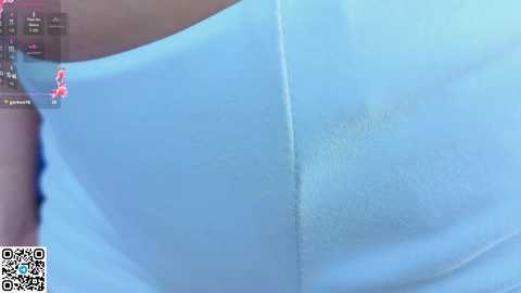A close-up video of a person's upper torso, showcasing their light blue, smooth, and slightly shiny skin. The image is grainy and blurry, suggesting a low-quality recording. A QR code is visible in the bottom left corner.