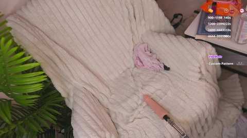 Video of a white, fluffy blanket with a pink toy and a USB stick on it, with green foliage in the background.