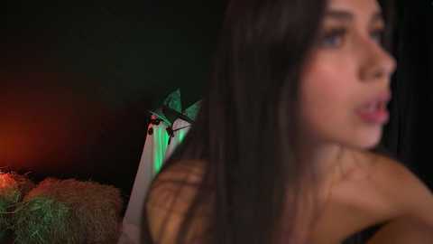 Video of a young woman with long black hair, brown skin, and dark eyes, partially blurred, standing next to a haystack with a green light shining.