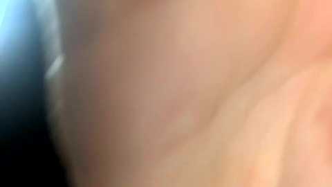 A close-up video of a pale, bare back with a soft, slightly blurred texture, showing skin folds and subtle shadows. The background is indistinct and dark.