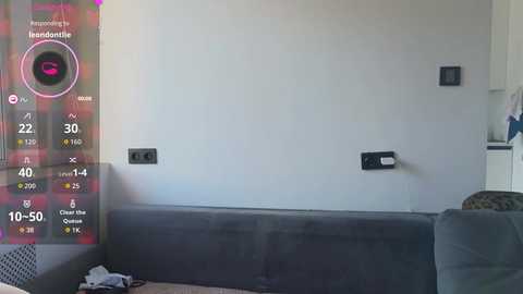 Video of a modern living room with a grey couch, plain white wall, black electrical outlets, and a colorful digital thermometer overlay.