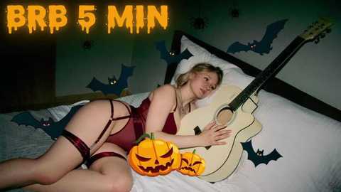 Media: Video of a blonde woman in red lingerie, lying on a bed with Halloween decorations and an acoustic guitar, with text overlay \"BBR 5 MIN.\