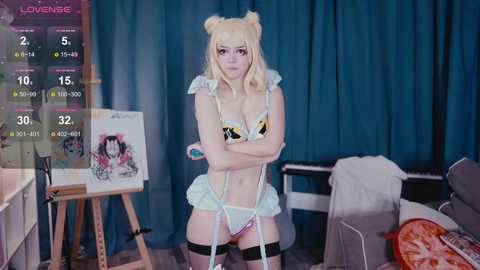 Video of a young woman in a catgirl cosplay, standing in a studio with blue curtains and a painting on an easel. She wears a yellow and black bikini with cat ears, black thigh-high stockings, and a frilly skirt.