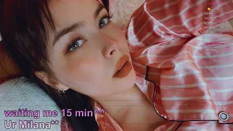 A close-up video of a young Asian woman with fair skin, brown hair, and light makeup, lying on her side, wearing a red plaid shirt. Text overlay reads, \"waiting me 15 min... Ur Milifana*\