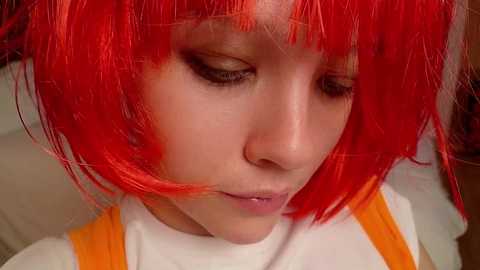 Video of a young child with bright red, shoulder-length, straight hair, wearing an orange and white dress, gazing downwards with a thoughtful expression.