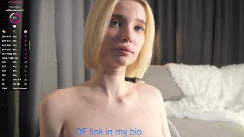 Media: Video of a topless, fair-skinned woman with a straight, blonde bob haircut, standing in a modern living room with grey curtains and a white fluffy couch. Text overlays the image: \"DF Link in my big.\