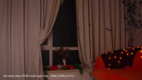 Video of a dimly lit room with beige curtains covering a window, a small table adorned with red apples, and a Halloween-themed orange couch with glowing orange lights.