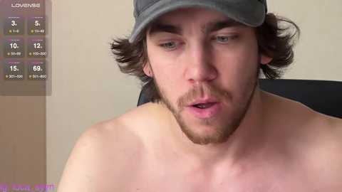 Video of a shirtless, light-skinned man with brown hair and beard, wearing a gray cap, looking surprised or confused. Background shows a weather app screen displaying temperature and weather icons.