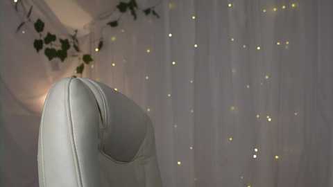 Video of a plush, white leather armchair with tufted upholstery in a softly lit room, adorned with white sheer curtains and twinkling fairy lights.