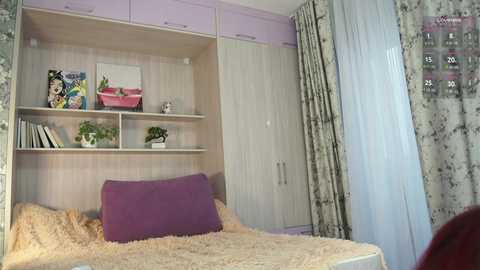 Video of a neatly organized bedroom with a light wood and pastel purple color scheme. The room features a bed with a fluffy beige blanket, a purple pillow, and a bookshelf with colorful books and plants.