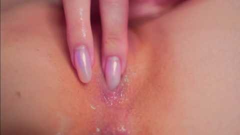 Close-up video of a woman's vulva, featuring light skin, slightly parted labia, and a hand with long, glossy pink nail polish gently touching the area.