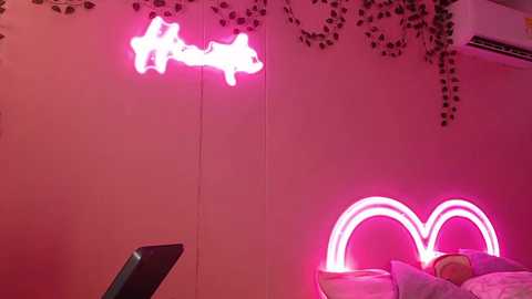 A video of a vibrant pink room with a neon heart-shaped light on the wall, a plush bear toy, and ivy decorations.