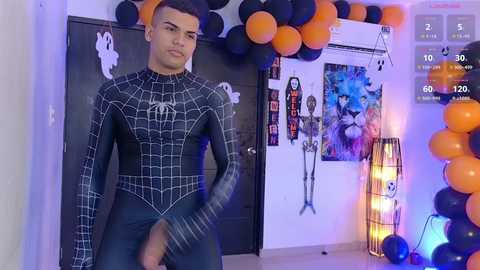 Video of a young man in a Spider-Man suit posing in a Halloween-themed room with decorations, balloons, and a digital clock showing 10:30.