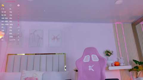 A video of a modern bedroom with white walls, a pink gaming chair, a white bed with a gold headboard, and framed minimalist artwork. Soft pink ambient lighting.