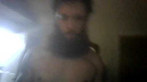 A blurry, dimly lit video of a person with shoulder-length dark hair and a full beard, wearing a dark shirt. The background is indistinct and shadowy, suggesting an indoor setting.