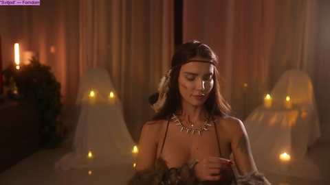 Media: Video of a woman in a dimly lit room with candles, wearing a sheer dress and feather headpiece, standing near a fireplace.