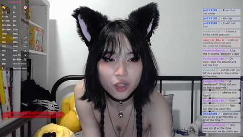 Media: Video of an Asian woman with black cat ears and collar, wearing a black bra, lying on a bed with a messy room background.