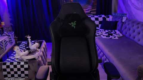 Video of a gaming setup with a black, ergonomic gaming chair in the center, surrounded by a checkered table and tufted gray couches under purple lighting.