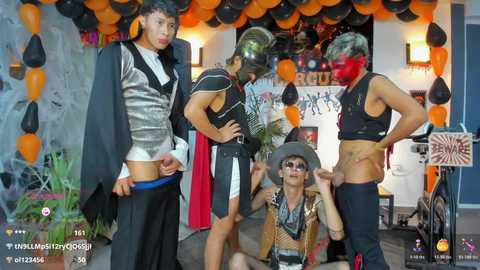A video captures a Halloween-themed party with four men dressed in black and white costumes, including a man in a hat and mask. The background features orange balloons, decorations, and a red curtain.