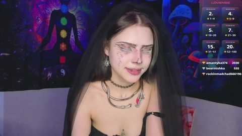 Media: Video of a pale-skinned woman with dark hair, wearing a black dress and multiple necklaces, with a trippy psychedelic background featuring a mushroom. She has white face paint and a serene expression.