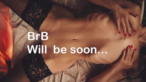 Video of a slender, topless woman with fair skin, wearing black lace lingerie, reclining on a bed. Her red-painted nails rest on her chest. Text overlay reads, \"BrB Will be soon...\