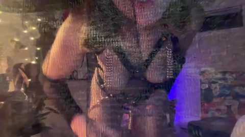 Media: Video of a woman in a sheer, black, lace bra, posing in a dimly lit room with warm lighting and a cozy atmosphere.