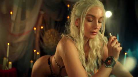 Video of a fair-skinned, blonde-haired woman in braided hair, topless, holding a lit pipe, in a dimly-lit, mystical room with candles and draped fabrics.