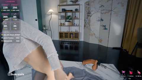 Video of a woman in a gray top and pants, bending over a desk, in a modern room with a map, shelves, and a lamp.
