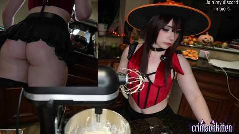 Video of a pale-skinned woman with short dark hair in a witch costume, wearing a red top, black skirt, and a large hat, mixing a bowl of white batter in a modern kitchen.