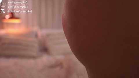 Video of a close-up view of a woman's bare backside, with dim, warm lighting, blurred background, and text overlay mentioning \"emilycampbell,\" \"cute campbell,\" and \"#TheEnvyCampbell.\