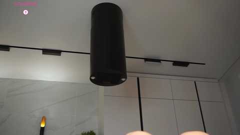 Video of a modern interior featuring a sleek, cylindrical black speaker hanging from the ceiling, against a white wall with built-in cabinetry and a marble countertop.