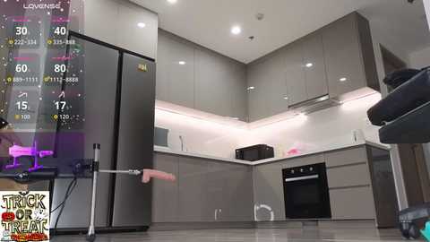 Video of a sleek, modern kitchen with gray cabinets, white countertops, and stainless steel appliances. A person, partially visible, stands holding a pink toy gun, with a \"Truck or Treat\" logo in the corner.