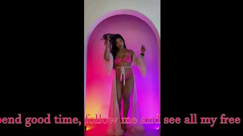 Video of a Black woman with long hair, wearing a pink lingerie set, standing in a pink-lit archway. Text reads, \"bend good time, follow me, see all my free.\