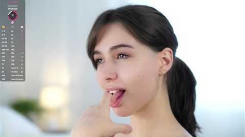 Media: Video of a young woman with fair skin and dark hair, sticking out her tongue. She's indoors, possibly in a bedroom, with a blurred background.