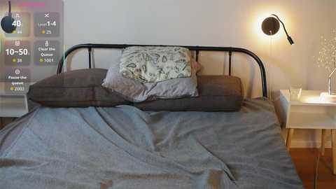 Media: Video of a modern, minimalist bedroom with a black metal bed frame, gray bedding, a patterned pillow, and a digital screen displaying sleep stats in the corner.