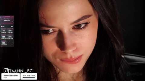 A close-up video of a woman with long dark hair, fair skin, and a slight frown. She has a small, fresh cut on her forehead, with a black and white overlay showing a Twitter post.
