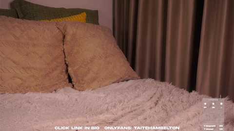 Media: Video of a neatly made bed with light beige pillows, a textured beige blanket, and a soft, shaggy white throw, set against a backdrop of brown curtains.