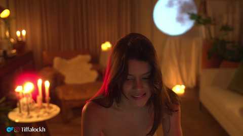 Video of a young woman with long dark hair, smiling, in a dimly lit room with candles, a full moon, and a cozy atmosphere.