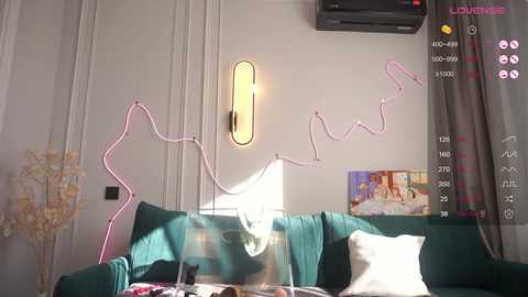 Video of a modern living room with a teal sofa, white pillows, a pink neon light wall sculpture, a framed anime poster, and a black air conditioner.