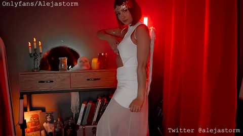A video features a woman in a white dress with a headband, standing against a red curtain backdrop. The room is dimly lit with candles on a wooden dresser.
