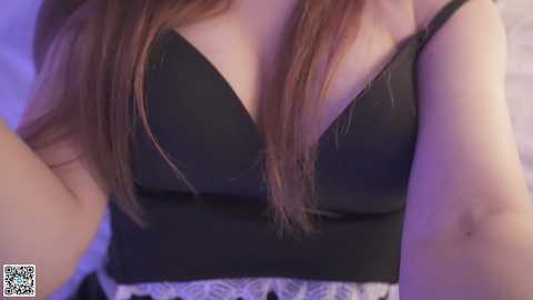 Video of a woman with fair skin and long, straight brown hair, wearing a black lace-trimmed bra, her cleavage visible.