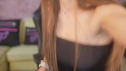 Blurred video of a woman with long, straight brown hair, wearing a black strapless top, in a dimly lit room with pink walls.