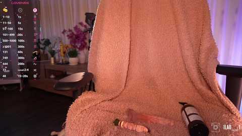 A video of a beige plush chair with a carrot toy and a bottle of wine on the seat, set in a dimly lit room with floral decorations and a TV showing a video feed.