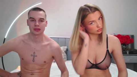 Video of a shirtless, tattooed young man and a blonde woman in lingerie sitting on a bed in a modern bedroom.