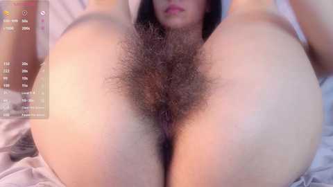 Media: A close-up, color video of a nude woman with a full bush of dark, curly hair, lying on her back with her legs spread, capturing her vulva.