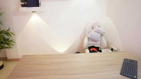 Video of a minimalist office setup with a white ergonomic chair, light wood desk, keyboard, and potted plant. The room has white walls and soft lighting, creating a clean, modern atmosphere.