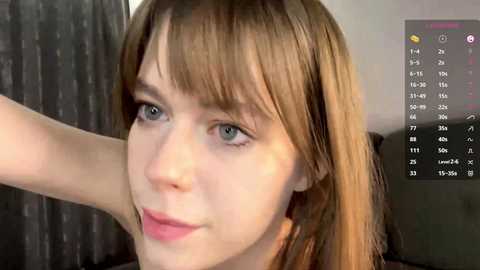 A close-up video of a fair-skinned woman with straight, light brown hair and blue eyes, wearing pink lipstick. She's indoors, with a calendar visible in the background.