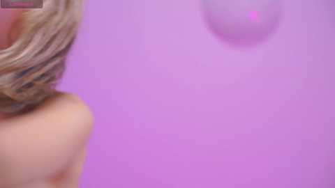 Video of a woman with fair skin and shoulder-length blonde hair, partially visible, standing against a solid lavender background. The image is soft-focused, creating a dreamy, ethereal atmosphere.
