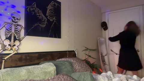 Video of a woman in a black dress, fleeing a room with a white door, decorated with a skeleton, cat, and plant.